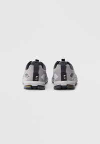 Une paire de chaussures de sport grises avec des onglets de talon noirs étiquetés "GTR" sur un fond blanc, vues de l'arrière.