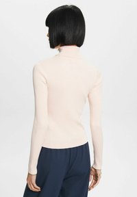 Suéter de cuello alto de color rosa claro, con textura de canalé, mangas largas y diseño ajustado. La vista trasera muestra una construcción sin costuras y un cuello alto.