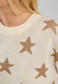 Maglione cremoso con grandi motivi a stella metallici dorati, colletto e polsini a costine, e un tessuto morbido e testurizzato.