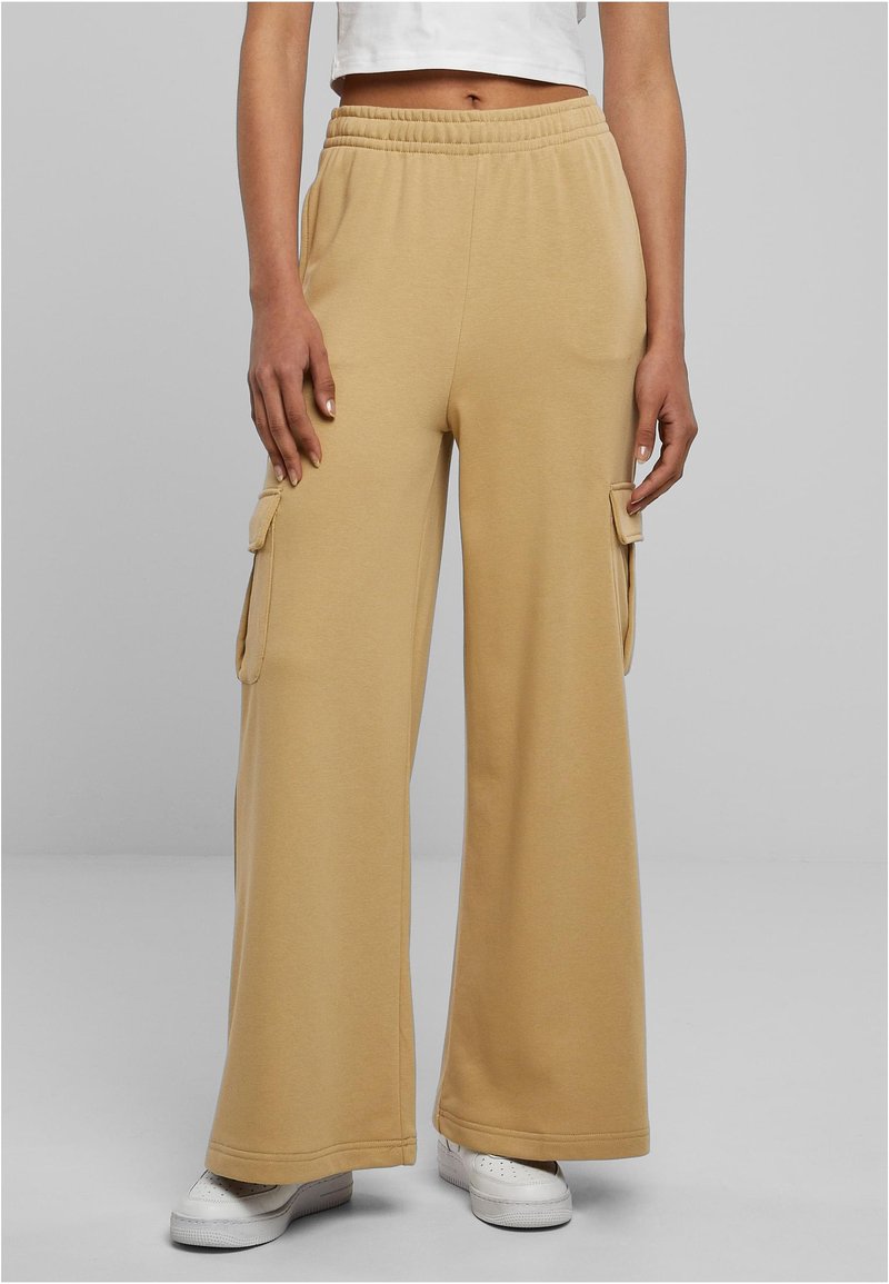 Beżowe szerokie spodnie dresowe z elastycznym paskiem w talii i bocznymi kieszeniami cargo. Materiał jest gładki i miękki, odpowiedni do codziennego noszenia.