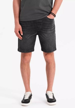 Shorts di denim neri con taglio classico, caratterizzati da una texture scolorita, design a cinque tasche e orli risvoltati. Indossati con sneaker bianche e nere.