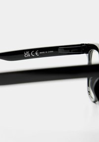 Čierne slnečné okuliare s plastovým rámom, s lesklými stranami. Nápis na vnútornej strane znie "CE MADE IN CHINA." Minimalistický design.