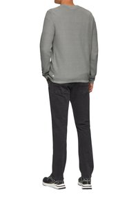 Grauer Strickpullover mit Rundhalsausschnitt, kombiniert mit schwarzen Jeans und sportlichen schwarzen Sneakers, von hinten betrachtet.