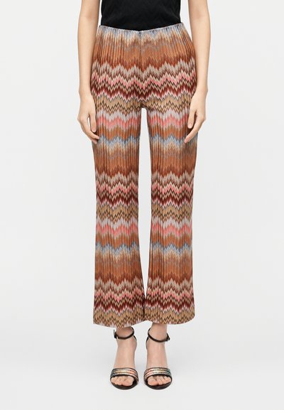 Pantalon à jambes larges marron à motifs zigzag multicolores, en tissu texturé avec une ceinture élastique. Associé à des sandales à talons noires.