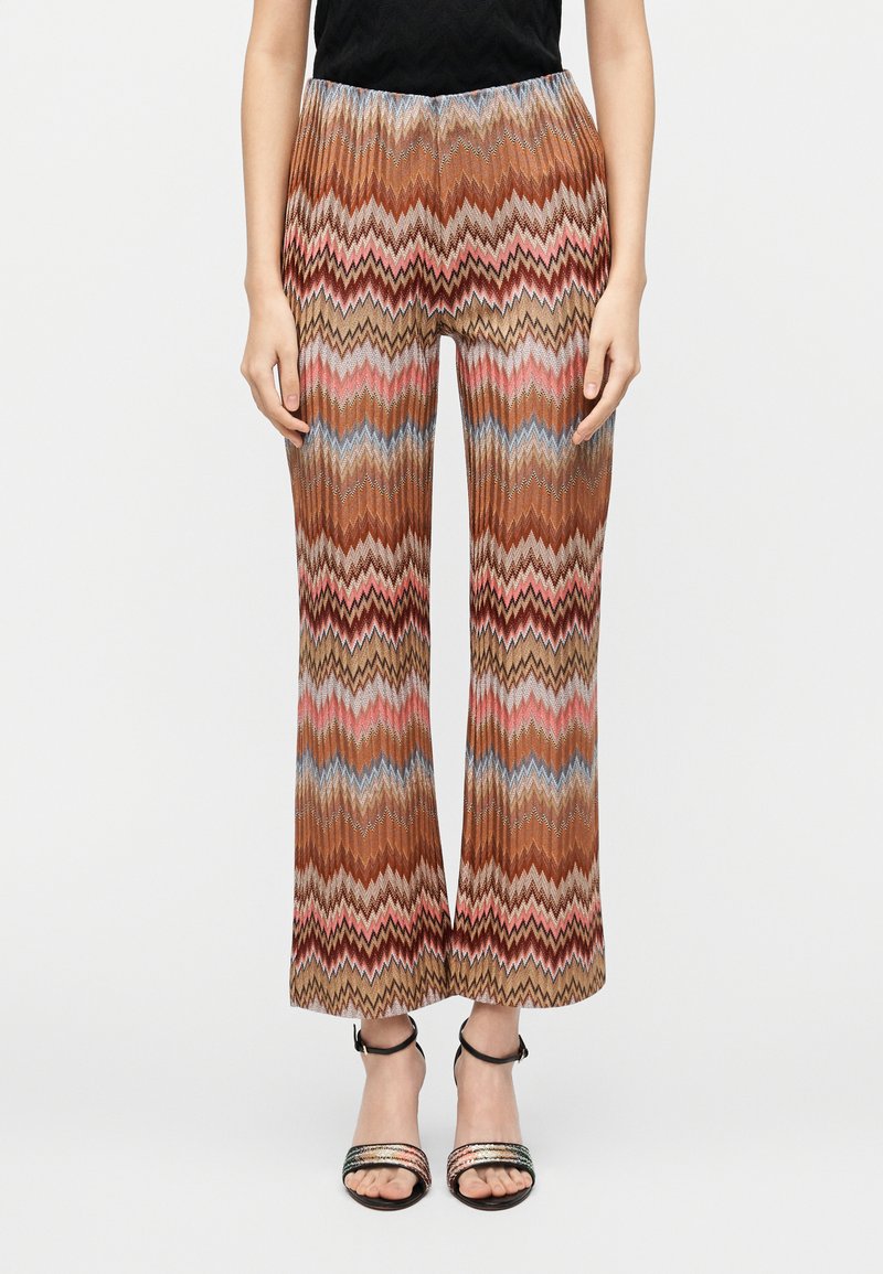 Pantalon à jambes larges marron à motifs zigzag multicolores, en tissu texturé avec une ceinture élastique. Associé à des sandales à talons noires.