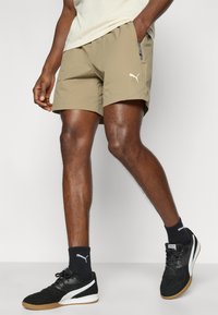 Σορτς ταμπακιέρας με πλευρική τσέπη με φερμουάρ και λευκή διακριτική στάμπα. Φοριέται με μαύρα αθλητικά παπούτσια και μαύρες κάλτσες σε αντίστοιχη σκιά.