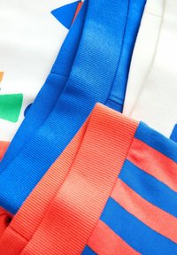 Campioni di tessuto colorati: blu a coste, rosso a righe, bianco e pattern geometrici in verde e arancione, che mostrano varie textures.