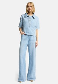 Lichtblauw denimoutfit bestaande uit een geknoopte korte mouwtop met kraag en brede broek; zachte textuur, losse pasvorm.