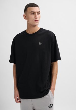 Schwarzes Baumwoll-T-Shirt mit rundem Ausschnitt und kurzen Ärmeln, ausgestattet mit einem kleinen weißen Logo auf der linken Brust, glatte Textur.