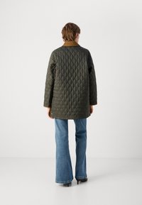 Gequiltede groene jas met een bruine kraag, met een middellange snit en lange mouwen, gecombineerd met flared blauwe jeans en zwarte hakken.