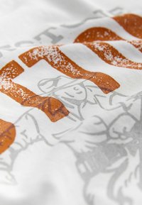 Valge kangast t-särk, millel on graafiline disain, kus on oranži ja halli värvi tekst ning illustreerimine, esitades tekstuuriga trükise, millel on lõdvestunud välimus.