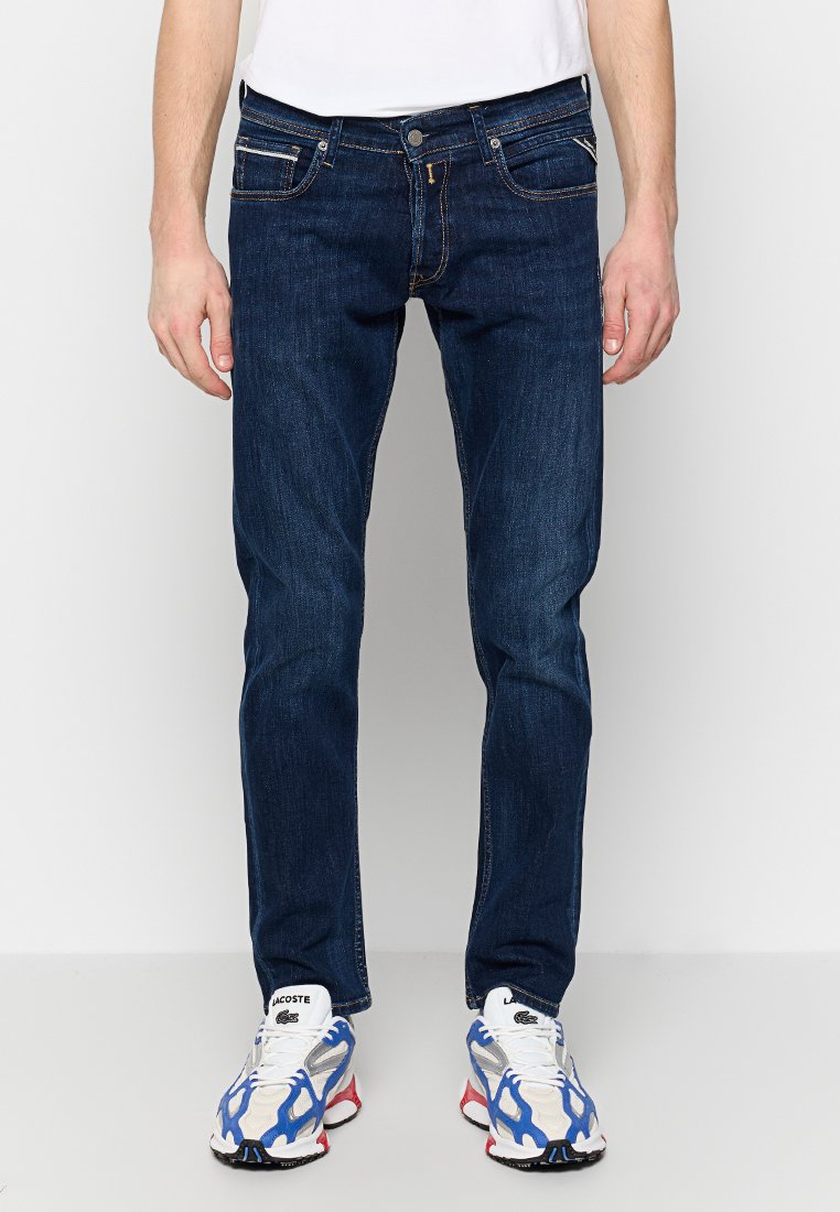 Jeans in denim blu scuro con vestibilità slim, dotati di tasche frontali, tasche posteriori e dettagli di cucitura a contrasto. Abbinati a sneakers multicolori.