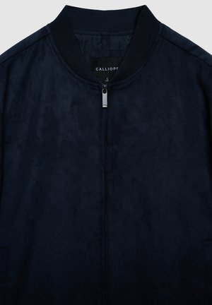 Marineblaue Bomberjacke mit glatter Textur, durchgehendem Reißverschluss und geripptem Kragen. Innen befindet sich ein schwarzes Etikett mit der Aufschrift "CALLIOPE."