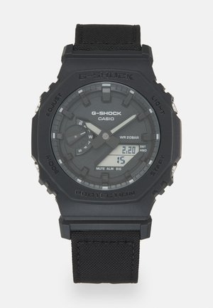 G-Shock klokke med en svart harpikshus og tekstilreim. Har digital skjerm og analog urskive, teksturert urskiveoverflate og flere urskiver.