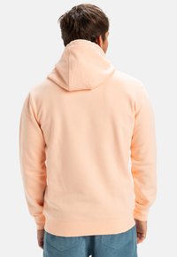 Light peach hoodie made of soft fabric, featuring a kangaroo pocket and adjustable hood. Ribbed cuffs and hem for a fitted look.