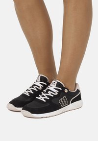 Schwarze und beige Sportschuhe aus Wildleder, mit weißen Schnürsenkeln, Logo-Akzent an der Seite und einer gepolsterten Sohle für Komfort.