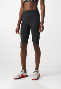 Pantaloncini sportivi neri con vita alta, caratterizzati da strisce diagonali testurizzate e un piccolo logo sulla gamba sinistra; abbinati a scarpe da ginnastica bianche e rosse.