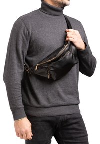 Borsa a tracolla in pelle nera con due scomparti conzip e tracolla regolabile, indossata a croce su un maglione a collo alto grigio scuro.