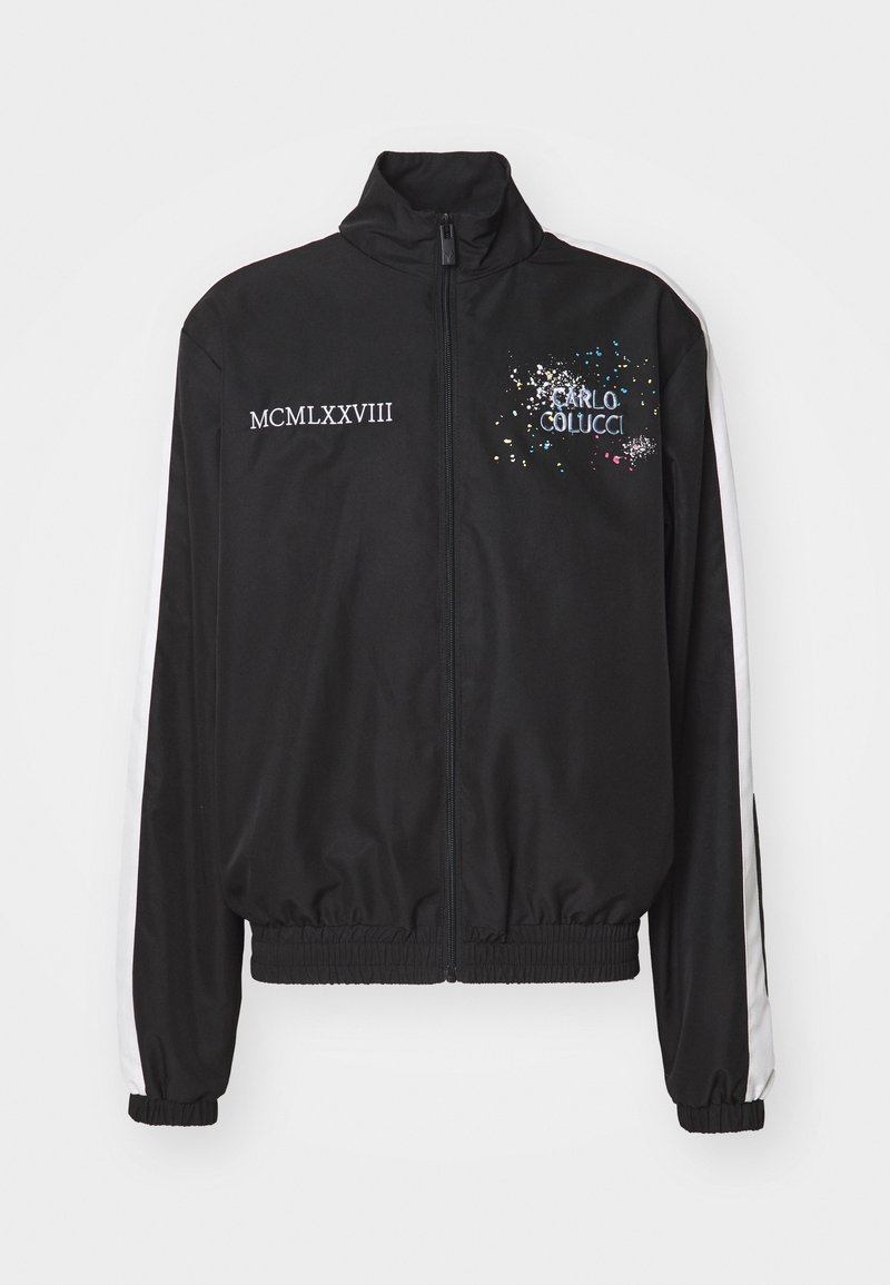 Chaqueta negra con cremallera, hecha de tela suave, con rayas blancas en los hombros, logotipo "Carlo Colucci" y texto "MCMLXXVIII" en blanco.