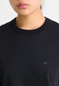 Camiseta de algodón negra con cuello redondo, que presenta un pequeño logo bordado en el lado izquierdo del pecho. Textura suave, ajuste estándar.