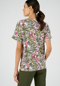 Camisa de manga corta con un colorido patrón floral que presenta hojas verdes y flores rojas sobre un fondo blanco, hecha de una tela suave.