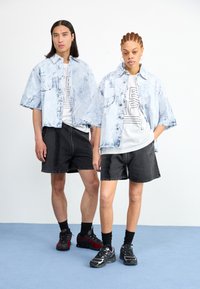 Lys blå denim oversized skjorter med frayed kanter, svarte grafiske t-skjorter, mørke shorts og atletiske sko i rød og svart farge.