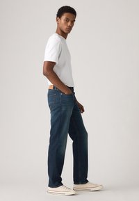 Tmavomodré džínsy z denimu s rovným strihom nohavíc, jemným vyblednutím a dizajnom s piatimi vreckami. Kombinované s jednoduchým bielym tričkom s krátkym rukávom.