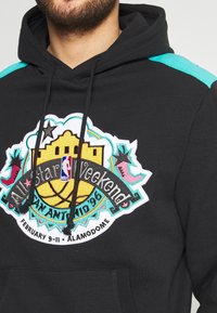 Schwarzer Hoodie mit türkisfarbenen Streifen, getragen von einem Mann, mit einem bunten NBA All-Star Weekend San Antonio 1996 Logo auf der Brust.