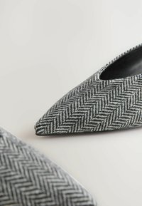 Pelēki herringbone raksta tekstila apavi ar izteiksmīgiem pirkstiem. Iekšpusē gluda melna apdare un plāna melna zole. Smalka tekstūra.