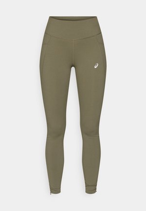 Leggings verde oliva con una texture liscia, vita alta, tasche laterali e dettagli con zip alle caviglie. Presenta un piccolo logo bianco.