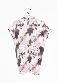 Haut à motif floral dans des tons de rose et de brun, avec une coupe ample, manches courtes et tissu doux. Suspendu à un crochet noir.