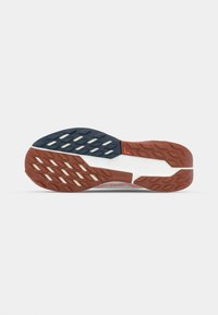 Trail running shoe outsole featuring red and navy rubber with multidirectional lugs for traction. Engraved logo and model details present.