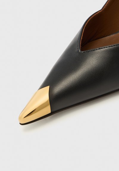 Scarpa nera in pelle con punta a punta e un accento metallico dorato sulla punta, caratterizzata da un design a intaglio lungo il bordo superiore.