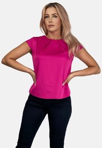 Dopasowany top z krótkim rękawem w jaskrawym różowym kolorze, z plisowaną przednią częścią. Zestawiony z ciemnymi, skinny jeansami. Gładki, błyszczący materiał.