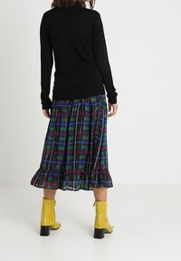 Svart långärmad topp tillsammans med en flerfärgad rutig kjol med volanger, kompletterad med ljusgula ankelskor med kraftiga klackar.