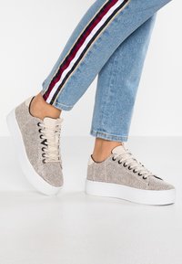 Baskets beiges avec un motif texturé, semelle en caoutchouc blanche et lacets en coton. Conception basse avec bout arrondi et œillets.