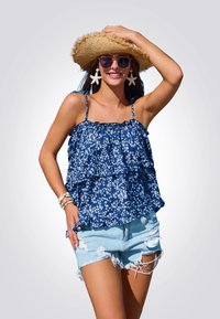 Blusa floral azul marino con volantes en capas, combinada con shorts de denim desgastados. Los accesorios incluyen un sombrero de paja y pendientes de estrella de mar.