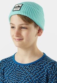Jasnoniebieska czapka z prążkowanego dzianiny z prostokątną czarną metką i białym napisem. Wzorzysty niebieski t-shirt z zygzakowymi wzorami.