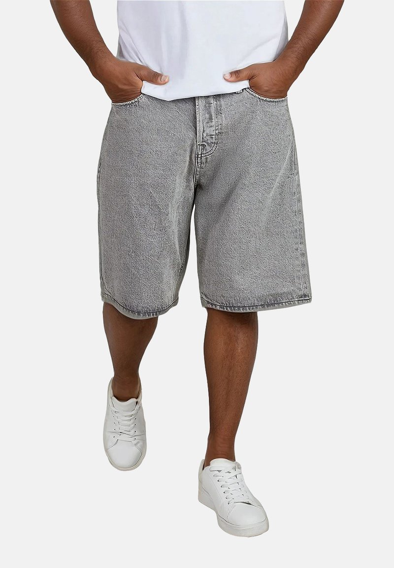 Shorts di denim grigi con una vestibilità comoda, dotati di tasche laterali, cuciture visibili e orlo dritto. Indossati con una maglietta bianca e sneakers.