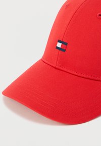 Κόκκινο βαμβακερό καπέλο baseball με καμπυλωτό γείσο, που διαθέτει ένα μικρό μπλε, λευκό και κόκκινο λογότυπο στην  μπροστινή πλευρά κοντά στην κορυφή.