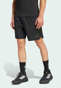 Pantalones cortos deportivos negros de material ligero, con una sutil abertura lateral, acentos texturizados en contraste y el logo de Adidas.