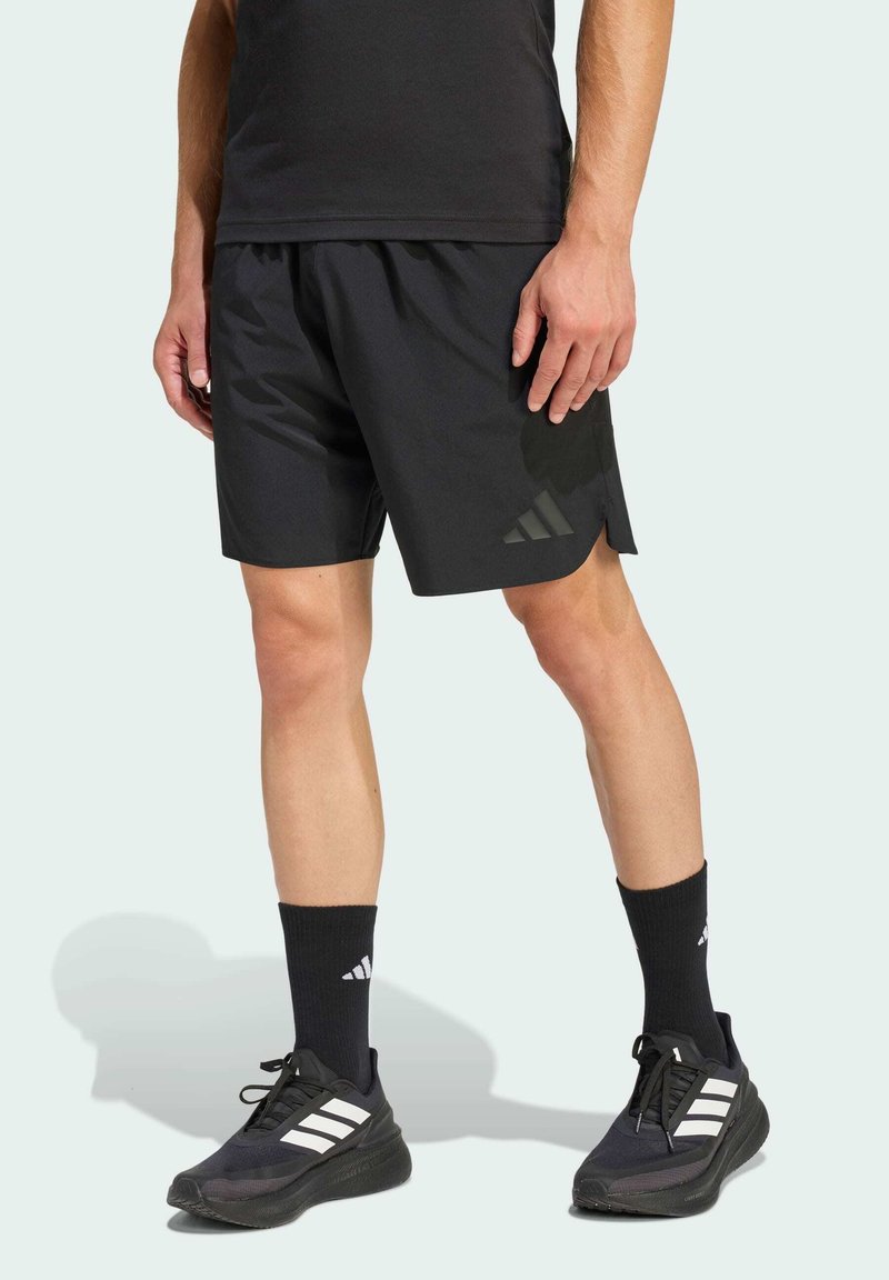 Pantalones cortos deportivos negros de material ligero, con una sutil abertura lateral, acentos texturizados en contraste y el logo de Adidas.