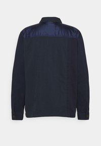 Tummansininen takki, jossa satiinin kaltainen kangas olkapäillä, napilliset kalvosimet ja kauluksellinen kaulus. Sileä pinta, jossa saumaviivat sivuilla.