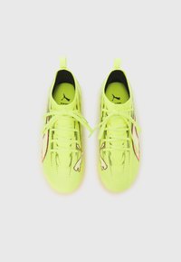 Felgele sportschoenen met een gestructureerd bovenwerk, veters en een gestileerde afbeelding aan de zijkant. Heeft een afgeronde neus en een lichtgewicht ontwerp.