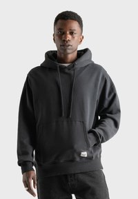Sudadera negra de algodón, con un bolsillo frontal, cordones y puños acanalados. Con un corte relajado y una pequeña etiqueta de logo.