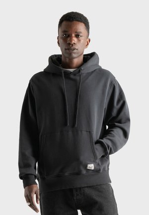 Black hoodie made of cotton, featuring a front pocket, drawstrings, and ribbed cuffs. Styled with a relaxed fit and a small logo tag.