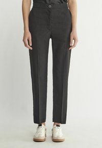 Svarta byxor med skräddarsydd design, slim fit, frontveck och en enkel knappstängning, tillsammans med vita sneakers.