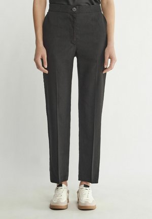 Pantalons noirs avec une coupe ajustée, des plis avant et une fermeture à un bouton, associés à des baskets blanches.