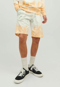 Szorty w technice tie-dye w odcieniach białym i brzoskwiniowo-pomarańczowym, z elastycznym paskiem w talii i sznurkiem do regulacji. Połączone z czarnymi trampkami i kremowymi skarpetami.