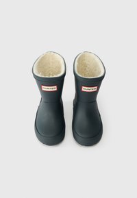Botas de borracha pretas com forro bege suave, apresentando um logótipo "HUNTER" em vermelho e branco na frente e sola texturizada para aderência.